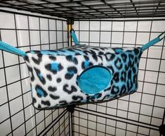 a leopard print cat bed hanging from the side of a cage in a room with tiled walls