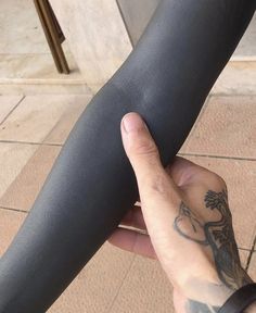 a person holding onto a black pole with tattoos on their arm and hand, in front of a building