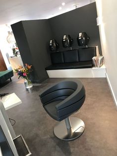 a black chair sitting in front of a window next to a vase with flowers on it