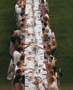 a group of people sitting around a long table with plates and glasses on it,