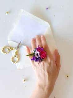 a woman's hand holding a flower ring on top of a piece of paper