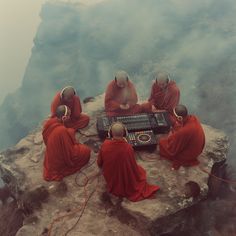 four monks sitting on top of a rock with headphones around their necks looking at an electronic device