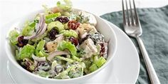 a white bowl filled with salad on top of a table next to a fork and knife