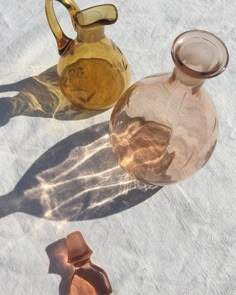 three different colored glass vases sitting on top of a white surface with shadows coming from them