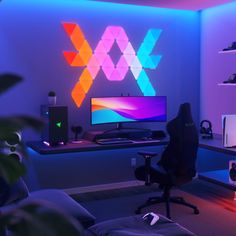 a computer desk with a monitor, keyboard and speakers on it in a room lit by neon lights