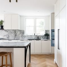 a kitchen with white cabinets and marble counter tops, an island in front of the sink