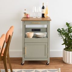 a kitchen cart with plates and wine bottles on it next to a potted plant