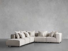 a white couch with pillows on it in front of a gray wall and concrete floor