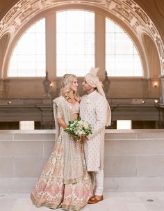 a bride and groom standing together in front of a large window