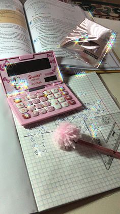 a pink calculator sitting on top of an open book next to a pencil