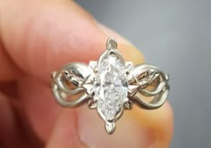 someone is holding an engagement ring with a diamond in it's center and leaves on the side