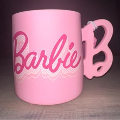 a pink coffee mug with the word barbie on it next to a pair of scissors