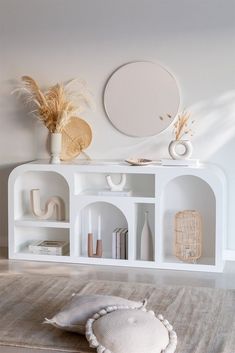 a white shelf with some decorative items on it and a round mirror above the shelves