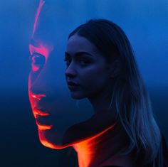 a woman standing next to a man with red light on his face in the dark