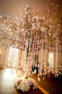 a tree decorated with white flowers and hanging from it's branches in a room