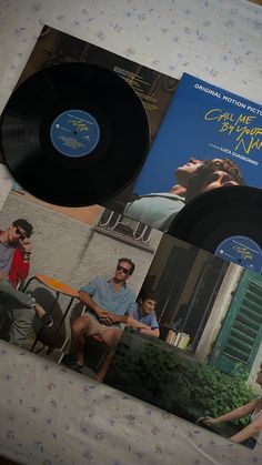 two black records sitting on top of a bed next to a magazine with an image of a man and woman