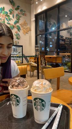 a woman sitting at a table with two cups of starbucks coffee