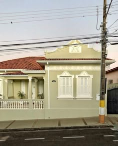 a house with white shutters on the front and red tiled roof, along side a street