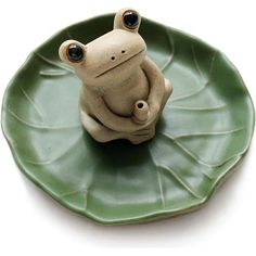 a small ceramic frog sitting on top of a green leafy plate with black eyes