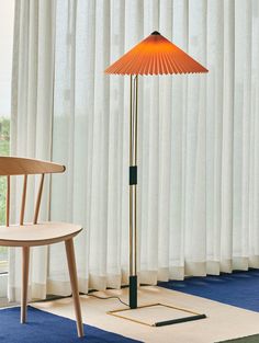 a floor lamp sitting on top of a blue rug next to a chair and window