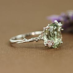 a close up of a ring on a table with flowers in the background and a purple flower