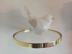 a small white bird sitting on top of a gold plated bangle holder,