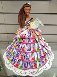 a doll made out of candy bars on top of a doily with a cake in the shape of a dress