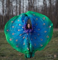 a woman in a peacock costume is holding up a large blue and green piece of cloth