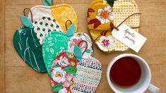 four oven mitts and a cup of tea on a wooden table next to each other