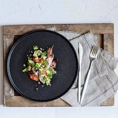 a black plate topped with meat and veggies next to a fork on top of a wooden tray