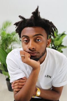 a man with dreadlocks sitting in front of a potted plant and looking at the camera