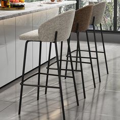 three bar stools sitting on top of a kitchen counter next to a bowl of fruit