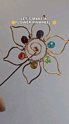 a hand holding a metal flower pin with colorful stones on it's center and the words let's make a flower pinwheel