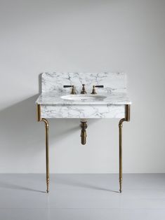 a white marble sink with gold legs and two faucets on the wall behind it