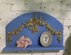 there is a blue shelf with some gold decorations on it and a pink flower next to it