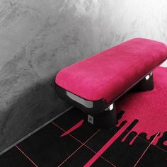 a pink bench sitting on top of a black and white floor next to a wall