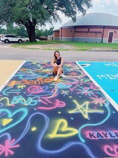 a woman kneeling on the ground in front of a chalk drawing