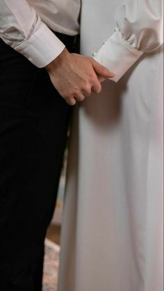 two people standing next to each other wearing white dresses and holding hands with one another