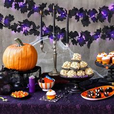 a table topped with lots of halloween treats and desserts next to a purple wall