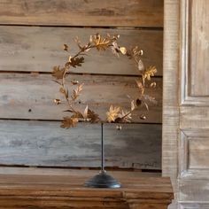 a gold leaf wreath on a stand in front of a wooden wall