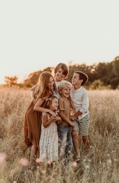 a group of kids hugging each other in the middle of a grassy field at sunset