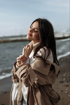 a woman standing on top of a beach next to the ocean holding her hands together