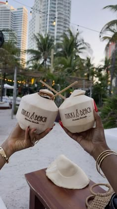 two women holding up coconuts in front of their faces with the city skyline behind them