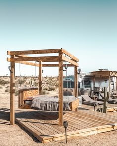 a bed sitting on top of a wooden platform in the middle of a dirt field