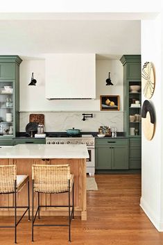 a kitchen with green cabinets and white counter tops, two wicker chairs at the island