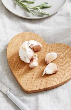 garlic cloves are on a heart shaped cutting board next to a knife and fork