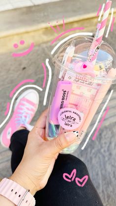 a person holding up a pink cup with straws in it and some writing on the side