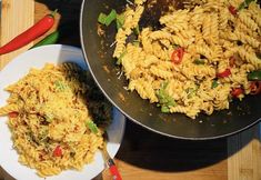 two plates with pasta and vegetables in them on a wooden table next to a spatula