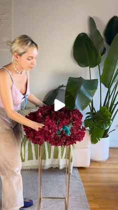 a woman is arranging flowers in a vase on a table with a plant behind her