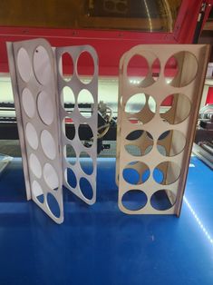 three metal racks with holes in them sitting on a blue countertop next to a red and white machine